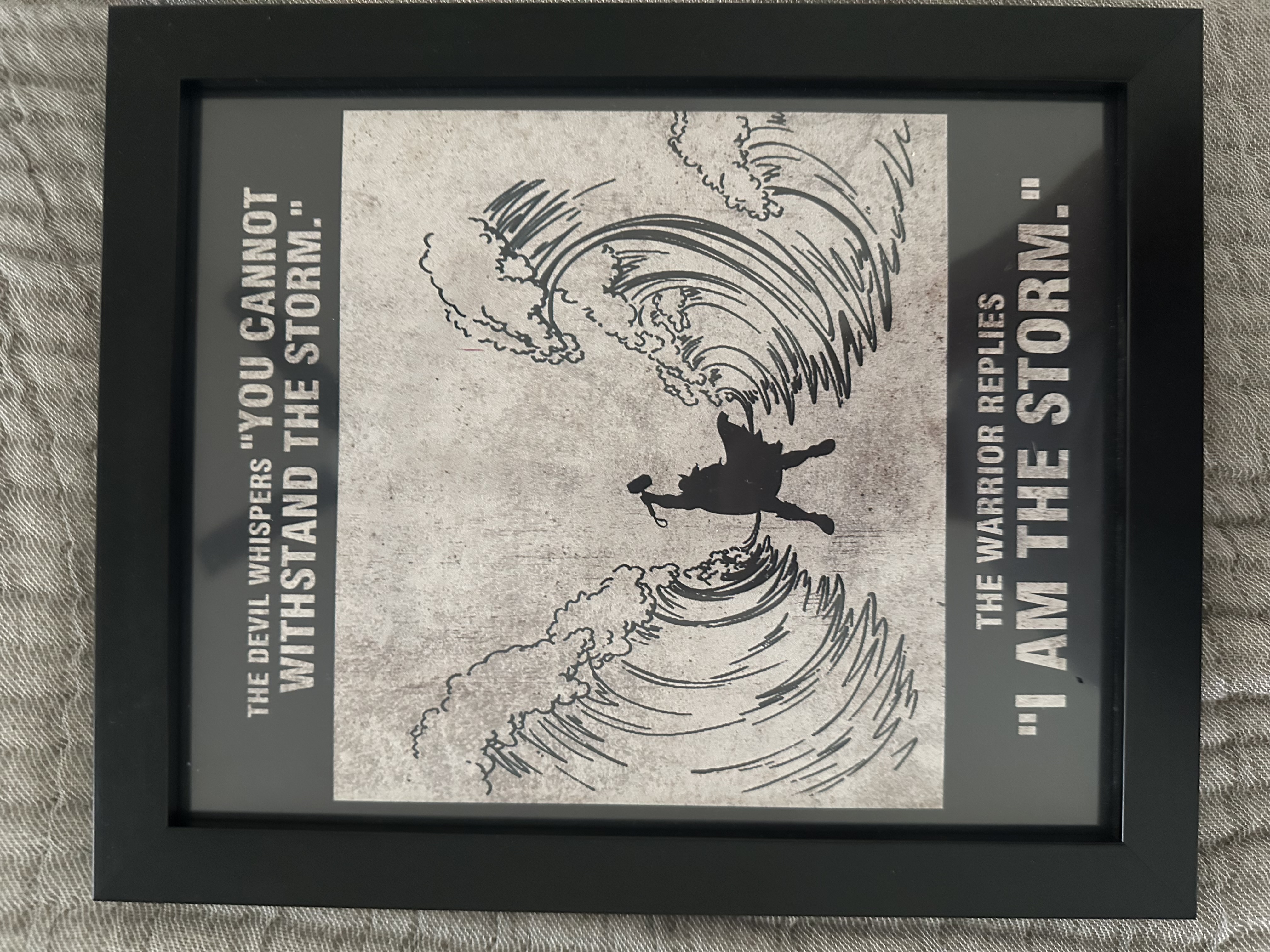 Framed artwork showing a warrior silhouette between two waves with text: The devil whispers 'you cannot withstand the storm.' The warrior replies 'I am the storm.'